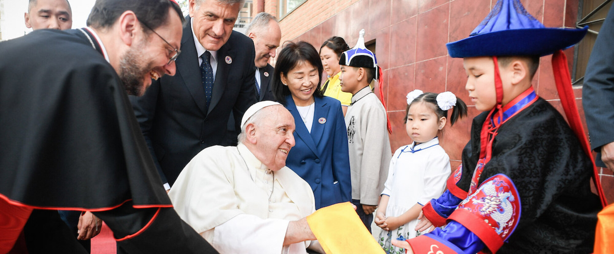 Kardinal Giorgio Marengo (l.), Apostolischer Präfekt von Ulan Bator, und Kinder in traditioneller Tracht, beim Empfang für Papst Franziskus am 1. September 2023 vor der Apostolischen Präfektur Ulanbaatar in Ulan Bator (Mongolei).